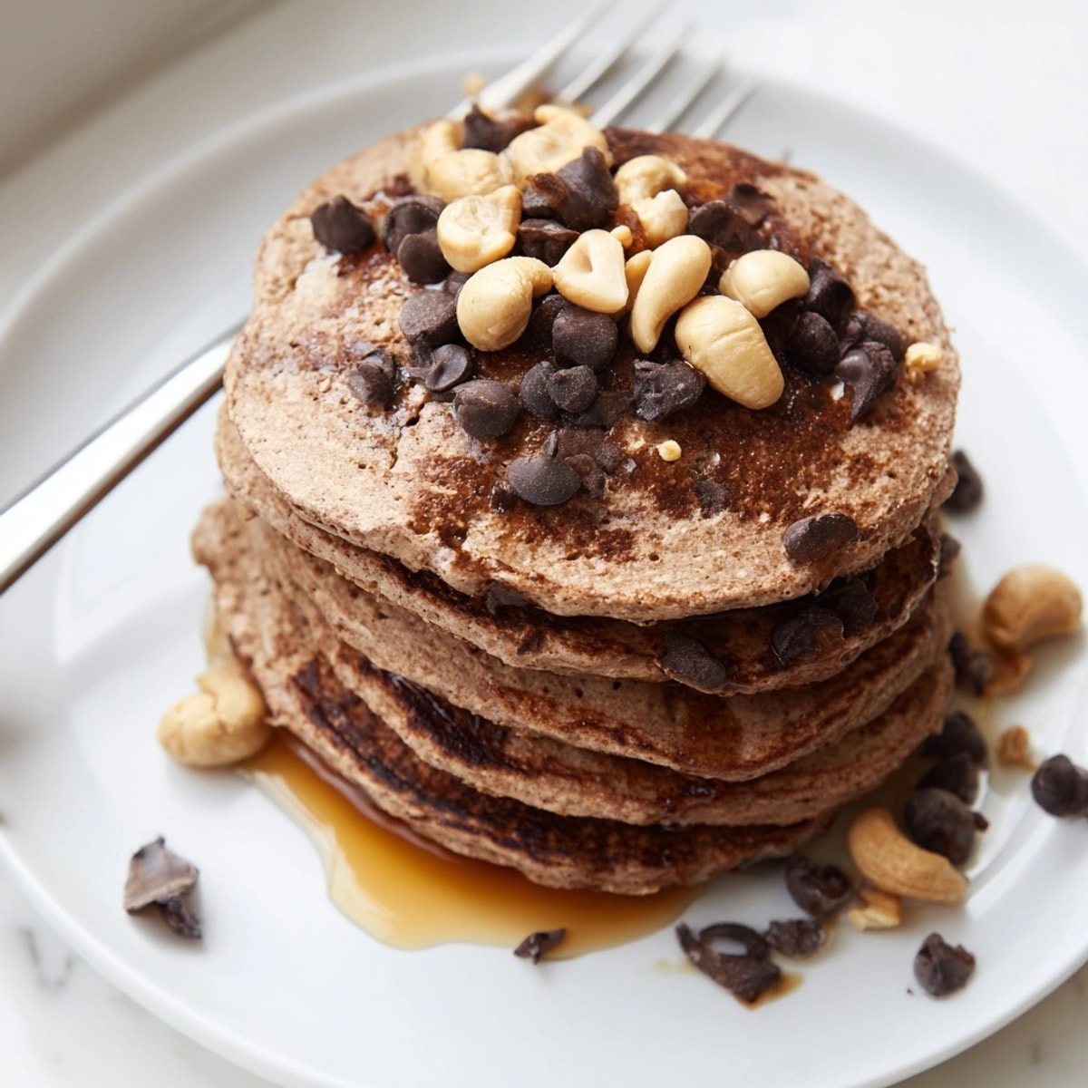 Stacked Protein Chocolate Cashew Pancakes, golden brown with visible cashew pieces, ready to eat.