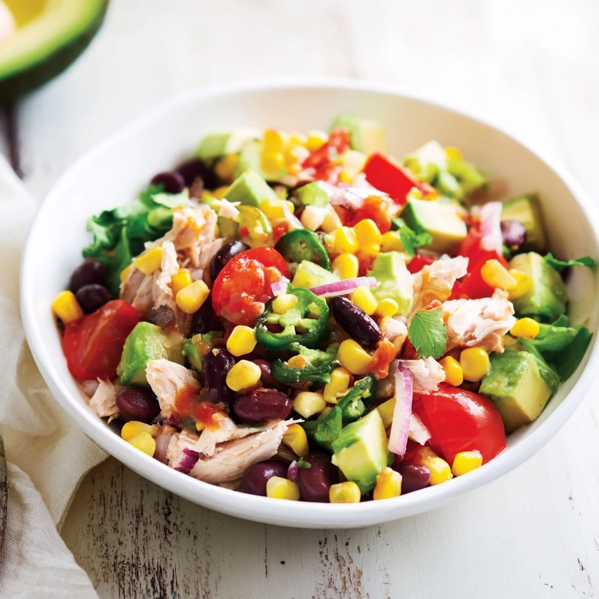 A bowl of delicious Dense Southwestern Bean Salad, full of juicy tomatoes, corn, and tender shredded chicken.