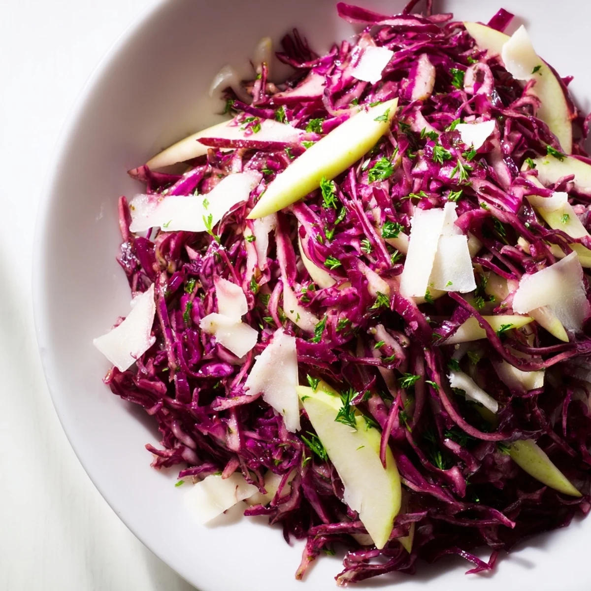 A close-up of vibrant red cabbage coleslaw with apple and Parmesan, glistening with tangy vinaigrette in a rustic serving bowl.