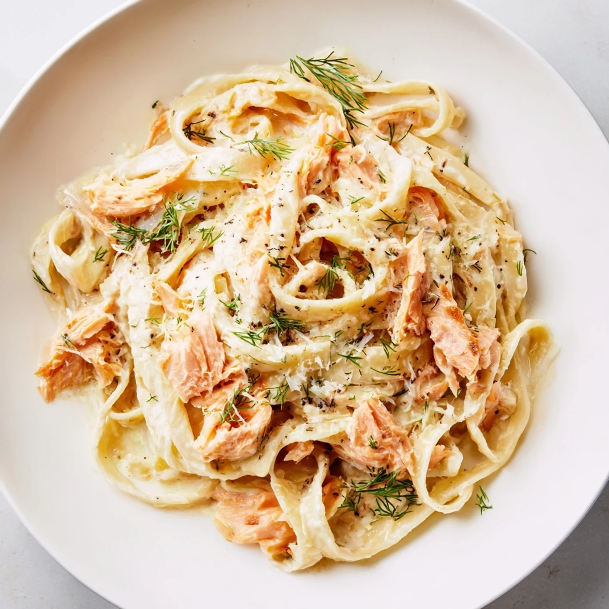 Silky creamy salmon pasta with lemon zest and dill, served on a white plate.