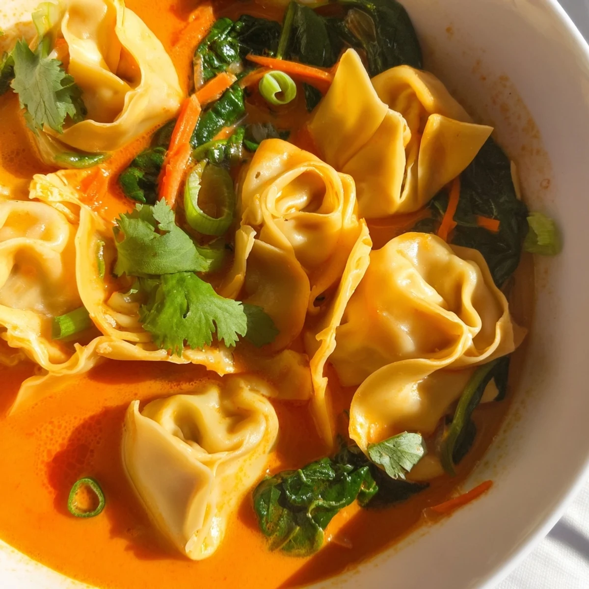 Golden-red curry broth with wontons, carrots, and wilted greens, garnished with scallions and lime.