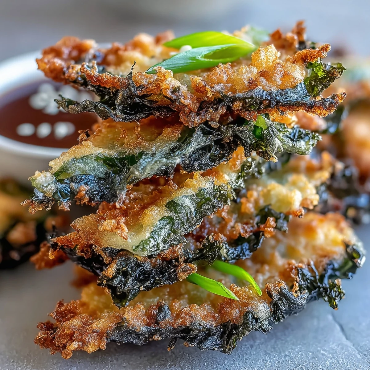 Golden-brown Seaweed Tempura pieces glistening with oil, stacked on a paper towel-lined plate next to a small ceramic bowl of dark dipping sauce.