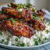 Sticky, glossy honey garlic BBQ sauce glistening on tender baked chicken wings served with savory buttered rice.