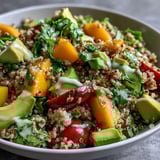 Spoonful of refreshing Tropical Mango Avocado Quinoa Salad featuring cherry tomatoes, red onion, and fresh cilantro on a rustic plate.