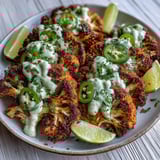 Thick Keto Chili Lime Cauliflower Steaks are plated with avocado crema, fresh cilantro, and lime wedges for a bright low-carb meal.
