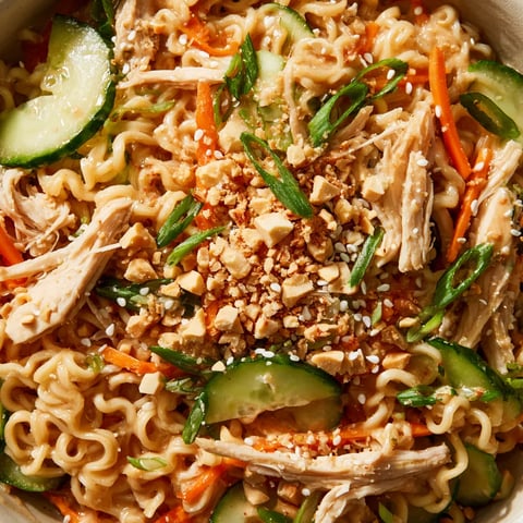 A bowl of noodles with chicken, cucumbers, and peanuts.