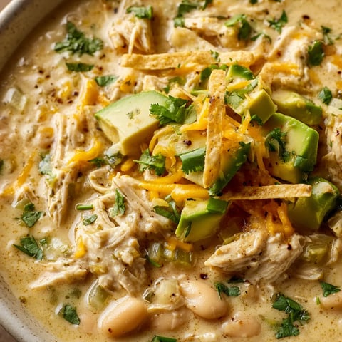 A bowl of chicken chili with cheese and avocado.