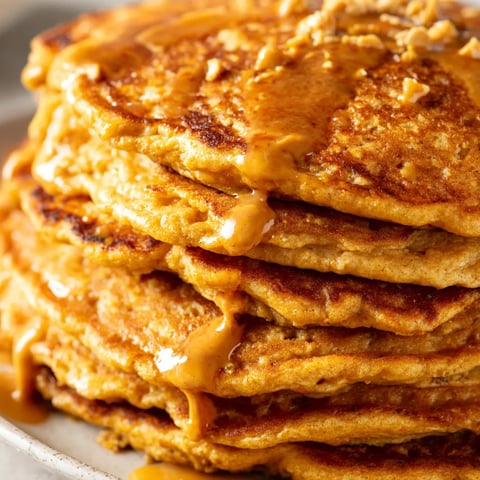 Pumpkin spice peanut butter pancakes stacked on a plate.