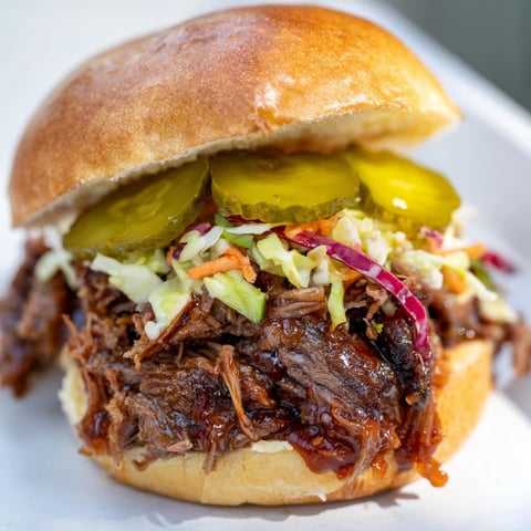 Smoky brisket slider tray with tender meat, bright slaw, and crunchy pickles on buns.
