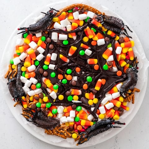 Dark chocolate spiderweb candy platter decorated with gummy spiders and colorful treats, perfect Halloween dessert.