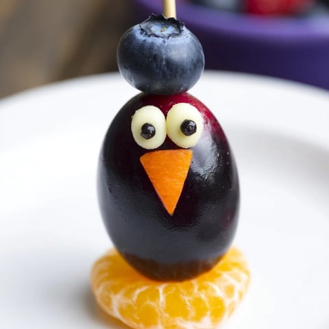 Plate of whimsical Penguin Fruit Skewer Army featuring colorful fruit and chocolate chip eyes.