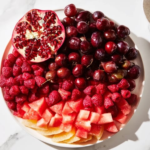 A colorful The Pomegranate Pivot fruit platter with juicy, sweet red and pink fruits arranged artfully.