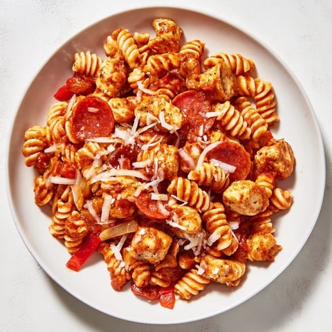A bubbling pan of One-Pan Pizza Pasta, cheese melted over rotini and chicken pieces.