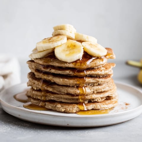 Golden-brown banana oat pancakes stacked high, ready to be drizzled with maple syrup.