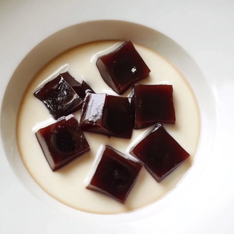 Cubes of Coffee Jelly Dessert in a glass, topped with sweet cream for a refreshing treat.