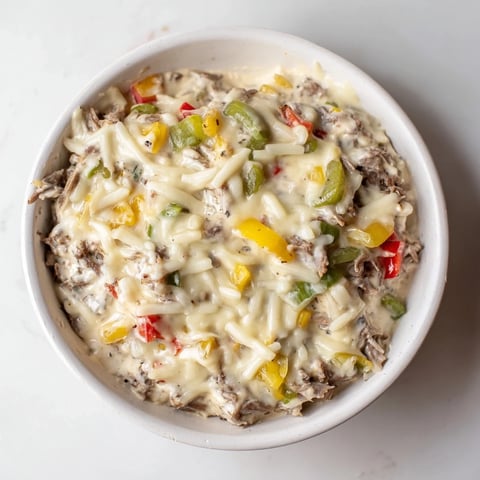 Golden-baked Philly Cheesesteak Dip in a dish, topped with melted provolone and served alongside crispy crostini.