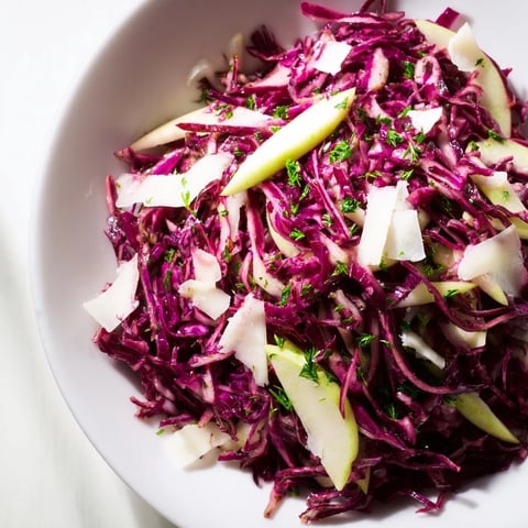 A close-up of vibrant red cabbage coleslaw with apple and Parmesan, glistening with tangy vinaigrette in a rustic serving bowl.