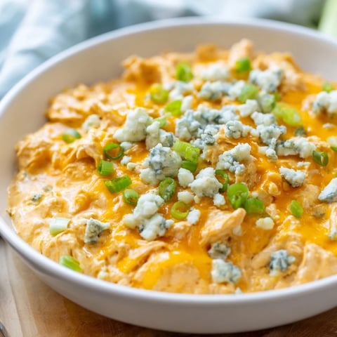 A warm and creamy bowl of Buffalo Chicken Dip, topped with melted cheddar and fresh green onions, perfect for dipping with tortilla chips.  