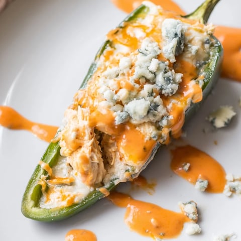 Four golden Buffalo Wing Poppers, stuffed with shredded chicken and blue cheese, resting on a rustic platter.