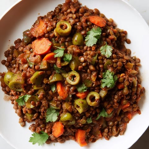 A steaming skillet of Cuban-Inspired Lentil Picadillo with lentils, olives, and sweet raisins, garnished with fresh cilantro.