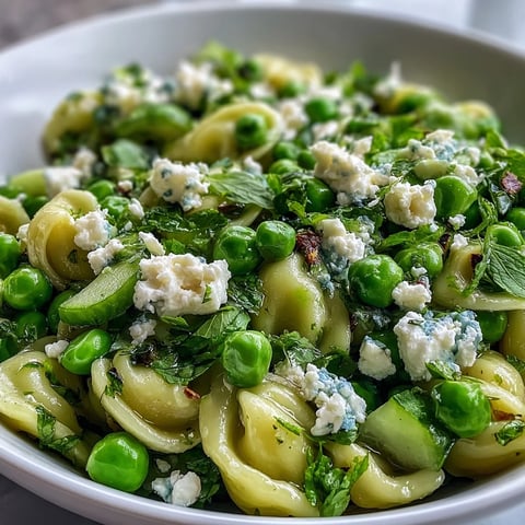 Fresh Spring Pea and Mint Pasta Salad in a white bowl, mixed with diced cucumber and sliced spring onions, drizzled with lemon vinaigrette.