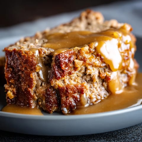 A slice of meatloaf with gravy on a plate.