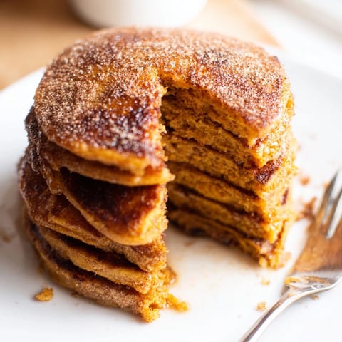 Stack of golden Cinnamon Sugar Sweet Potato Pancakes dusted with sweet cinnamon spice.