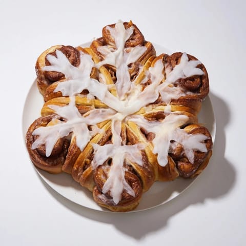 A close-up of a warm, frosted Giant Snowflake Sweet Roll, fragrant with cinnamon and vanilla.