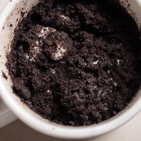 A single serving Oreo Mug Cake, rich chocolate with visible Oreo cookie pieces, ready to eat.