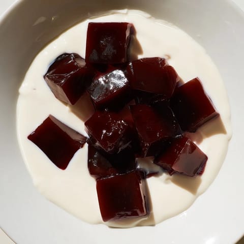 A close-up of Coffee Jelly Dessert, showcasing the wobbly coffee cubes and creamy topping.