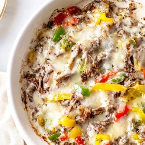 A warm, bubbly bowl of Philly Cheesesteak Dip with sautéed peppers and onions peeking through the cheesy topping.