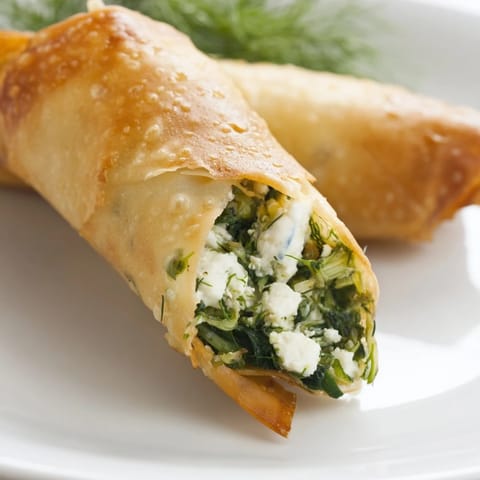 Spanakopita Spring Rolls sizzling in hot oil, revealing crispy golden wrappers and savory spinach-feta filling.  