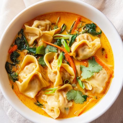 Creamy Thai-inspired Red Curry Wonton Soup With Greens ladled into a white bowl, steam rising.