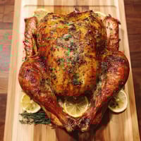 A roasted turkey with herb butter on a wooden cutting board.