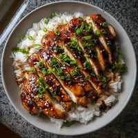 A plate of grilled teriyaki chicken with rice.