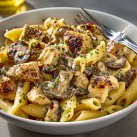 A bowl of pasta with chicken and mushrooms.