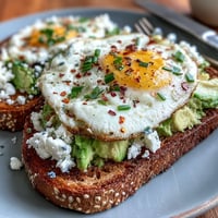 Fluffy egg white and creamy avocado spread on toasted whole grain bread, garnished with fresh herbs and a chili flake kick.