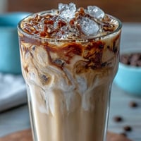 Refreshing protein iced latte smoothie in a tall glass, topped with a swirl of foam and a sprinkle of cinnamon.