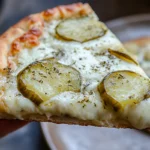 Close-up of a slice of pickle pie pizza with melted mozzarella and dill pickles.